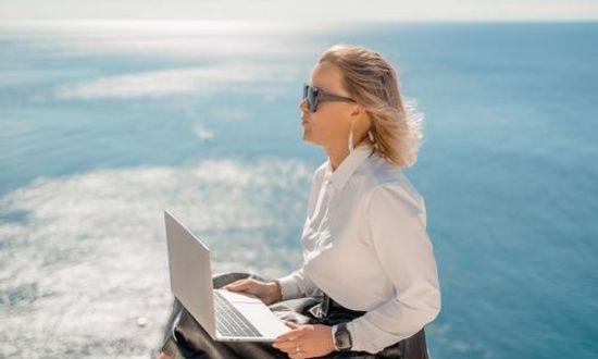 Female digital nomad with laptop overlooking the sea